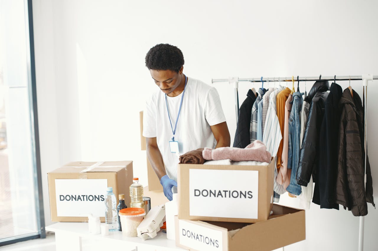 services-03 A volunteer organizes donations in a community center, featuring boxes labeled "Donations" and a clothing rack.