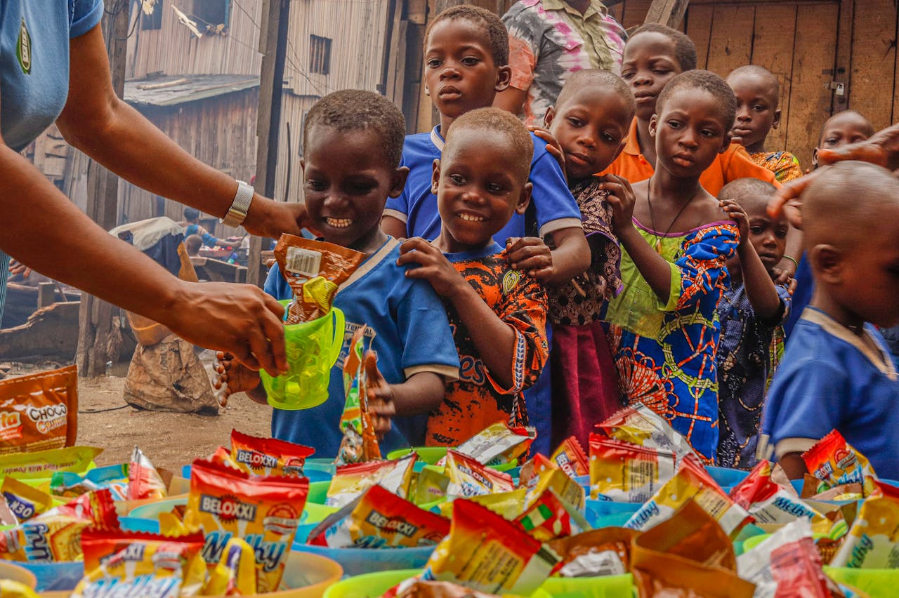 hero-img-01 Joyful children receiving food supplies from a volunteer in an outdoor setting.